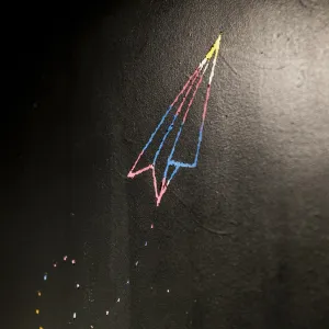 Detail of a drawn paper airplane made of colorful lines flying up the wall