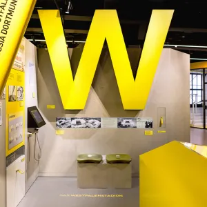 Teil der Ausstellung mit zwei Sitzplätzen aus dem Westfalenstadion patziert unterhalb einem größen gelben Leuchtbuchstaben, einem W