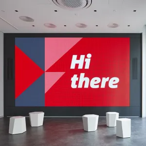 Wall-filling screen with text: Hi there and triangular graphic elements in the brand colors red and grey, in front of the screen are seats made of small white stools