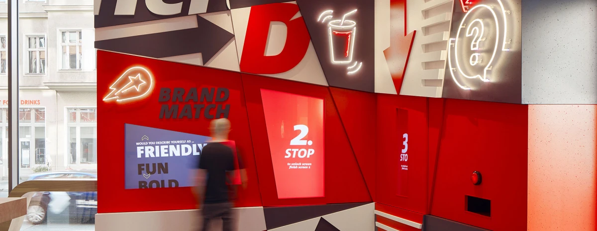 Interactive wall in the Delivery Hero welcome area, with screens for a brand quiz and various decorative asymmetrical elements in the brand colors