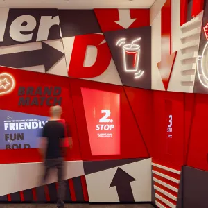 Interactive wall in the Delivery Hero welcome area, with screens for a brand quiz and various decorative asymmetrical elements in the brand colors