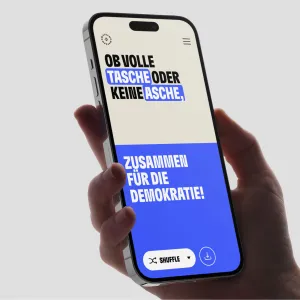 Smartphone Screen, eine Hälfte in Beige, eine in leuchtendem Blau, der Satz: Ob volle Tasche oder keine Asche, zusammen für die Demokratie! steht in kontrastreicher Schriftfarbe auf dem jeweiligen Hintergrund.