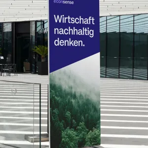 Freestanding display in the econsense design in blue and green tones, with a nature motif and the claim “Rethinking the economy sustainably.”