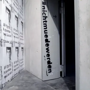 Ausstellungsraum mit Durchgang, im Türrahmen ist der Titel der Ausstellung 