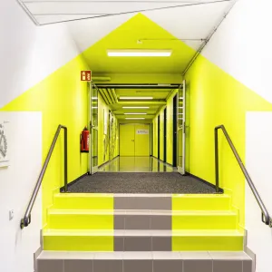 From the right angle, the neon yellow painted surfaces in the entrance corridor reveal the customer logo, a house and an arrow