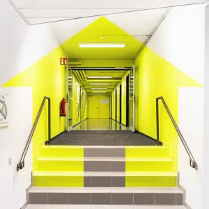 Aus dem richtigen Blickwinkel ergibt sich aus den neongelben gestrichenen Flächen im Eingangsflur das Kundenlogo, aus einem Haus und Pfeil