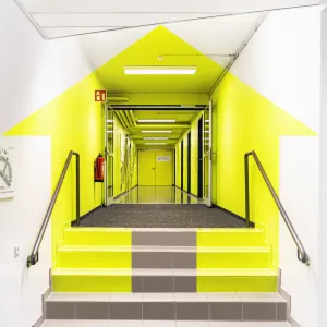 From the right angle, the neon yellow painted surfaces in the entrance corridor reveal the customer logo, a house and an arrow