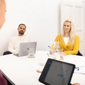 Fotoshooting mit drei Mitarbeitenden von MPW Immobilien, die um einen Konferenztisch sitzen, während einer der Mitarbeitenden etwas erklärt