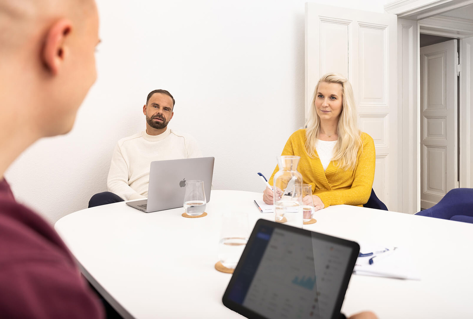 Fotoshooting mit drei Mitarbeitenden von MPW Immobilien, die um einen Konferenztisch sitzen, während einer der Mitarbeitenden etwas erklärt