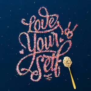 Elaborately ornate text made of sprinkles: Love yourself, with a spoon with cookie dough lying next to it