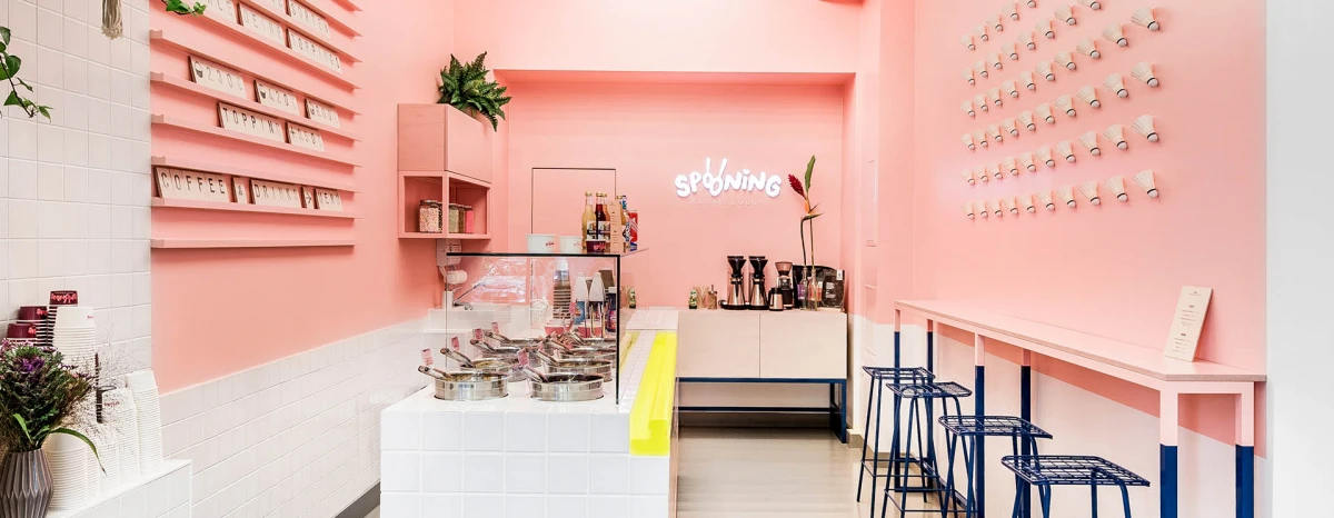 Store with pink walls and decorative dark blue details, there is a neon yellow armrest along the counter