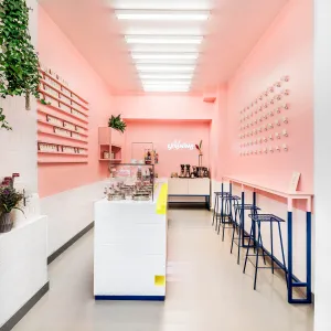 Ladengeschäft mit rosanen Wänden und dekorativen dunkelblauen Details, an der Theke entlag befindet sich eine Neongelbe Armablage