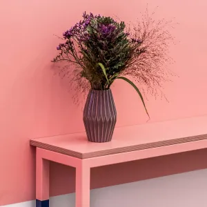 Narrow pink table along the pink store wall, in the foot area of the dark blue bar stools the wall is painted light, at the same height as the color change on the wall, the table legs are painted in dark blue