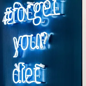 Glowing blue lettering: #forget you diet, placed on a dark blue wall