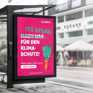 Plakat an einer Bushaltestelle, weißer Text Iss vegan für den Klimaschutz und einem illustrierten Pinsel, der anstatt Borsten Rucolablätter hat