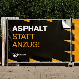 Black-and-yellow construction fence banner with the catchy headline “Asphalt Instead of a Suit”
