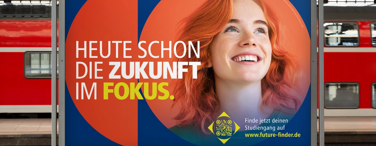 A billboard on a platform, with a train on the track in the background. The main motif can be seen on the poster. The red-haired woman with an orange background in a geometric shape on a dark blue background. Above it is the headline of the first campaign phase. Focusing on the future today.